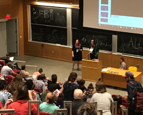 Two people address crowd of people in an auditorium